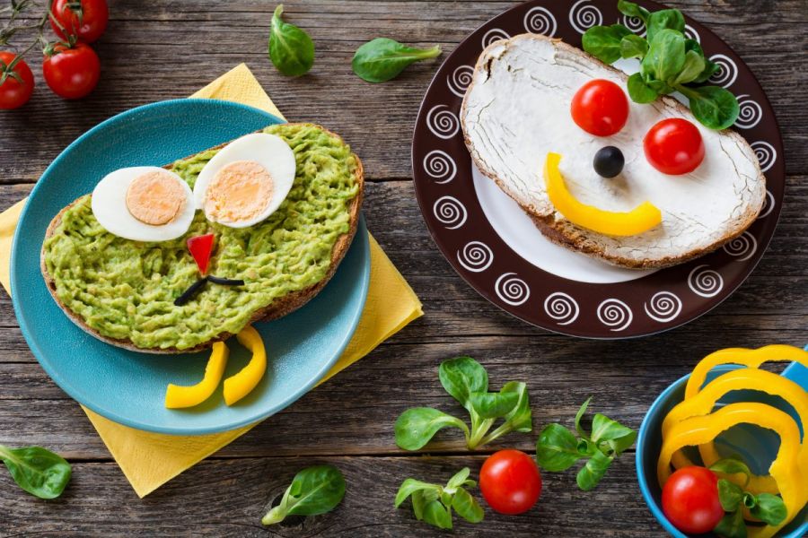 Two open sandwiches for kids, one with mashed avocado and hard boiled egg and other with cream cheese and vegies.