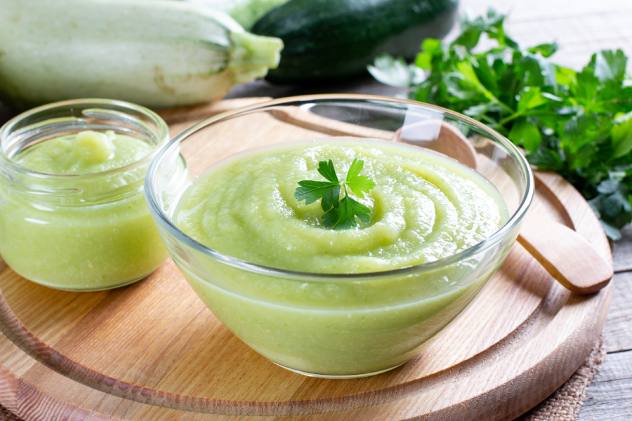 Zucchini puree in a glass jar with fresh zucchini on the background.