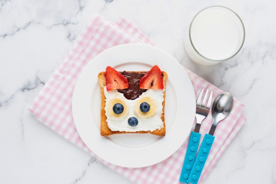 A square slice of bread with fruit and spreads as an animal face.