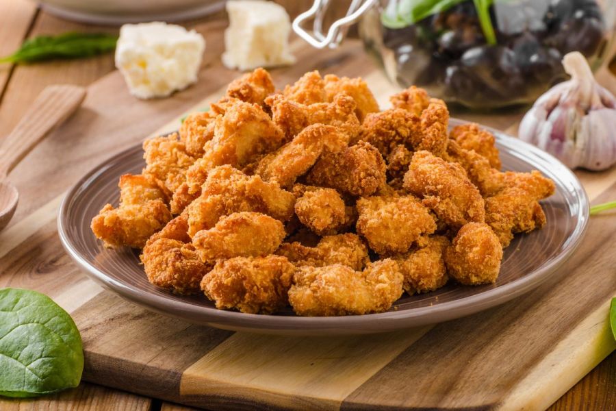 A plate of homemade popcorn chicken with a Greek salad on the background.
