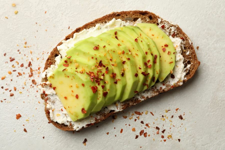 Toast with cream cheese, sliced avocado, and red chili flakes sprinkled on top.